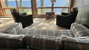 A living room with a large window offering a view of the sea. There are two black armchairs and a sofa with plaid upholstery. A wooden coffee table is in the center. - Dockside Retreat Limit 14 5 Bedroom Home (Sebago)
