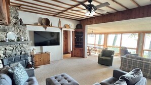 A spacious living room with a large sectional sofa, ottomans, a stone fireplace, a flat-screen TV, and a wooden ceiling with exposed beams. - Dockside Retreat Limit 14 5 Bedroom Home (Sebago)