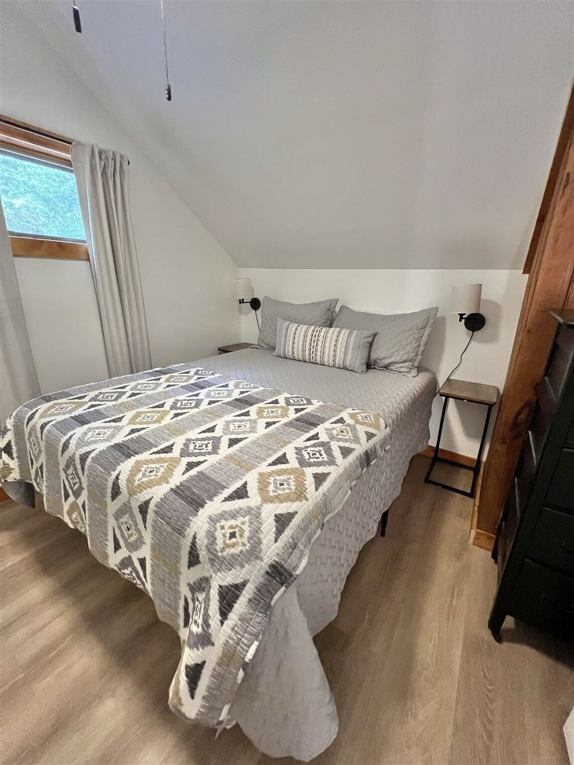 A bedroom with a bed, a nightstand, a lamp, and a window with curtains.