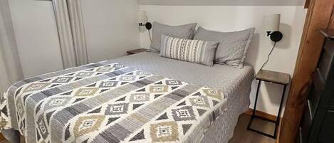 A bedroom with a bed, a nightstand, a lamp, and a window with curtains.