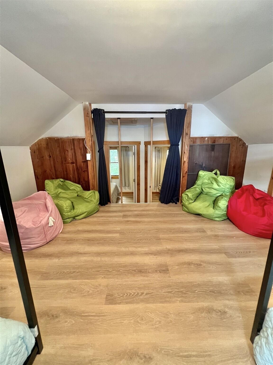 A room with a sloped ceiling, wooden flooring, and a view through a door. There are bean bags in green, red, and pink colors.
