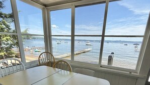 Una habitación iluminada por el sol, con una mesa grande y sillas, y amplias ventanas que dan a vistas del mar y barcos.