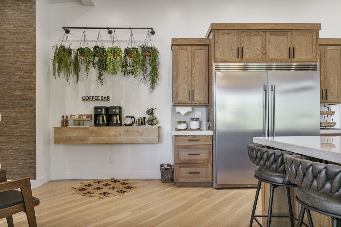 A modern kitchen with wooden cabinets, a stainless steel refrigerator, a hanging plant display, and a coffee bar area.