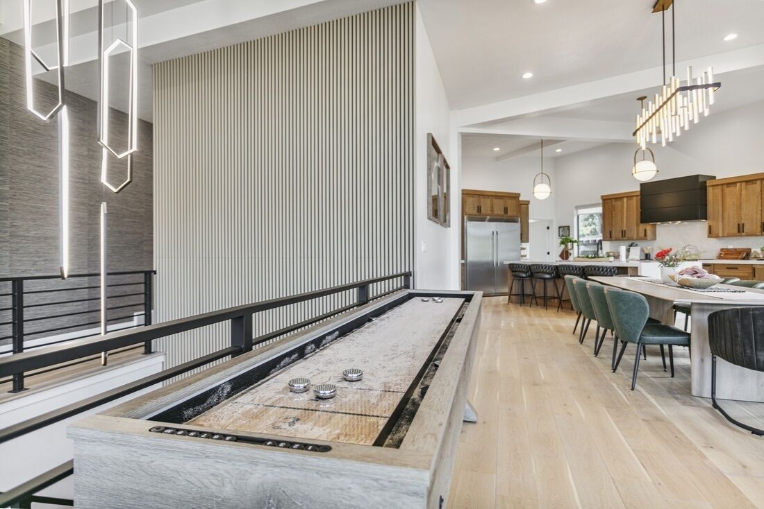 A modern kitchen with a long dining table, wooden cabinets, and pendant lighting.