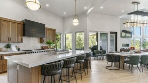 Een ruime keuken met een groot eiland, houten kastjes en moderne verlichtingsarmaturen.