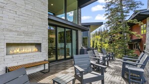 Een modern terras buiten met een stenen muur, een ingebouwde vuurplaats en zitplaatsen.