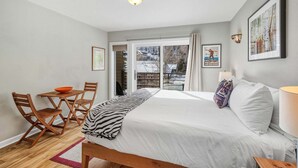 Ein Schlafzimmer mit Bett, Tisch mit Stühlen, Fenster mit Blick auf eine verschneite Landschaft und einer Tür, die nach draußen führt.
