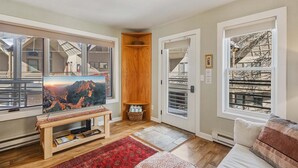 Ein Wohnzimmer mit großem Fernseher, einer hölzernen Bank, einem roten Teppich und Bergblick durch die Fenster.