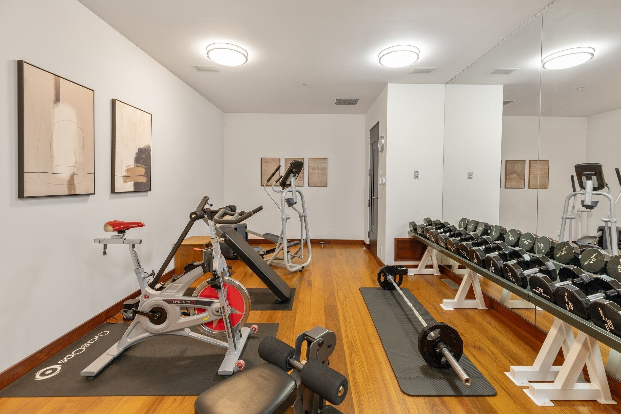 A gym with exercise equipment, including a stationary bike, elliptical, and weight bench.