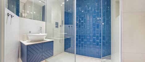 A modern bathroom with a glass-enclosed shower, a white sink, and a blue geometric cabinet.