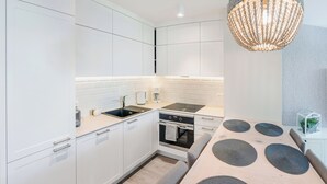 Et moderne køkken med hvide skabe, indbygget ovn, kogeplade og en hængende lampe.