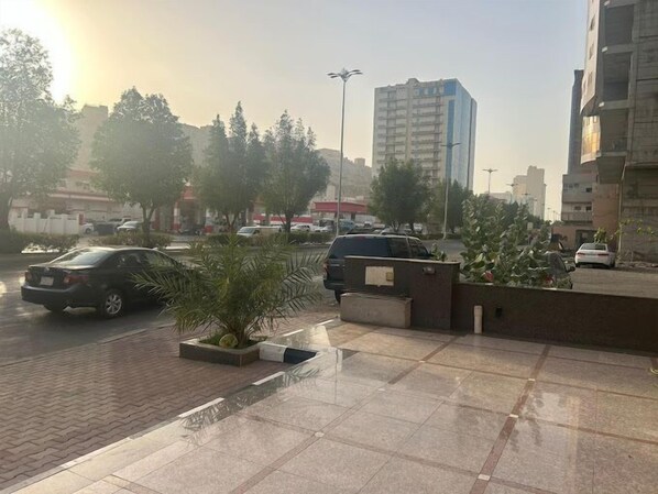 A parking area with cars, a palm tree planter, and a building in the background. - Blue Pearl Hotel (Makkah)