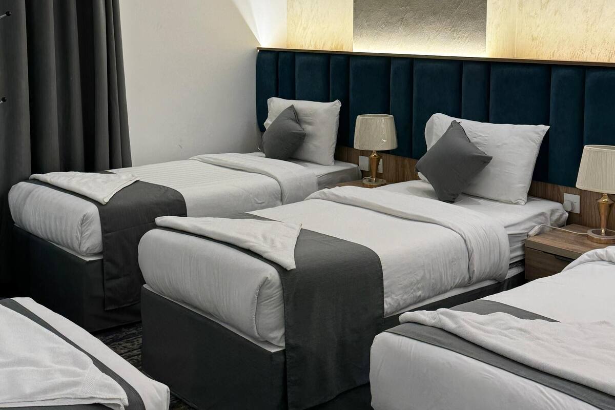 A hotel room with two beds, a large window with curtains, a marble wall, and a modern headboard.