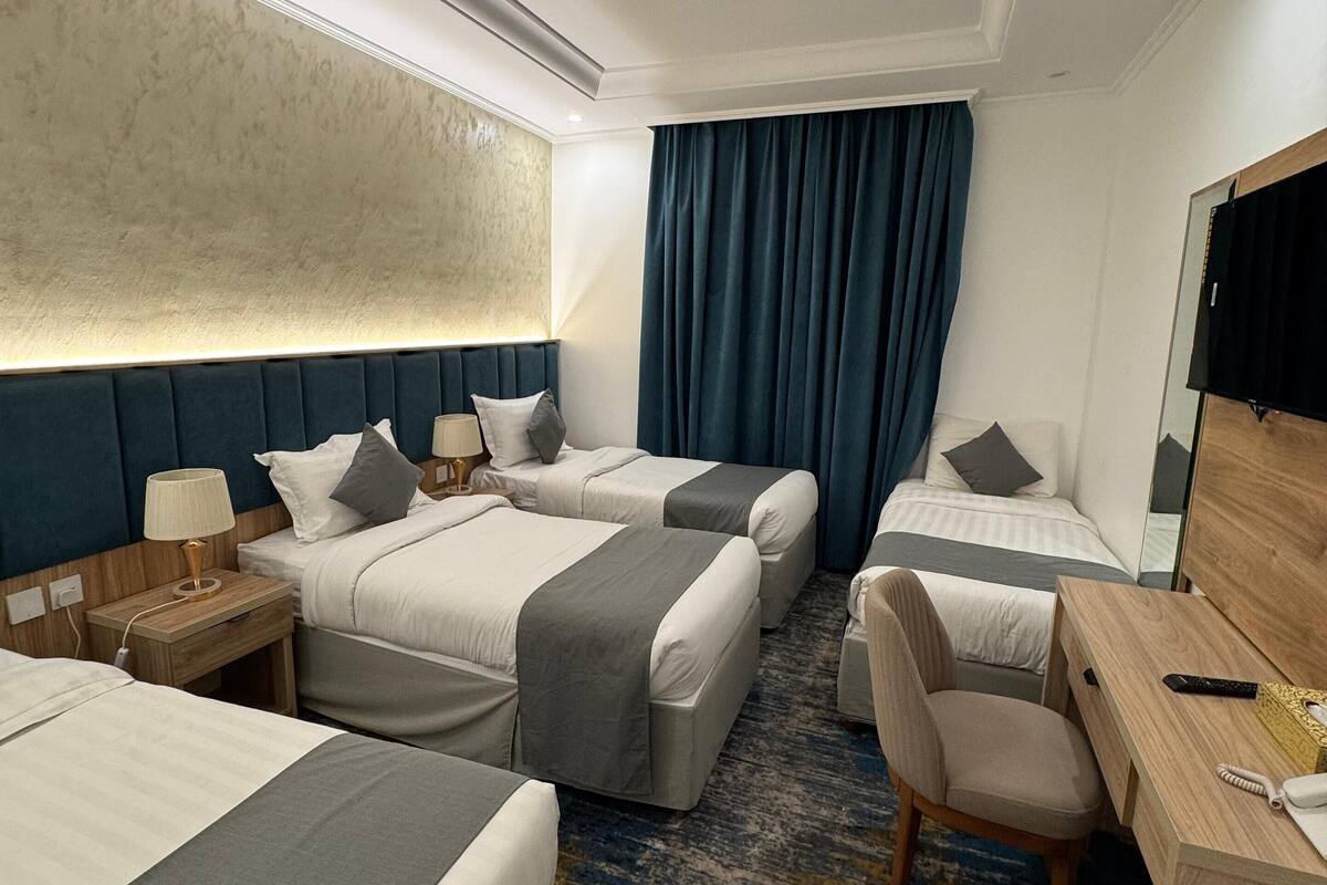 A hotel room with two beds, a desk, a chair, a TV, and a large window with curtains.