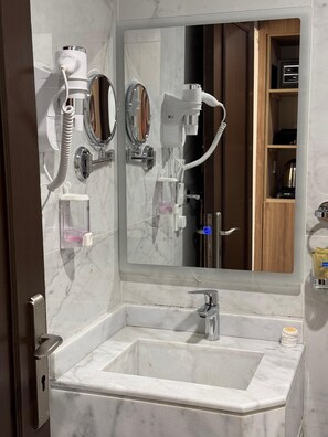 A bathroom with a marble sink, two mirrors, a hairdryer, and a towel dispenser. - Blue Pearl Hotel (Makkah)