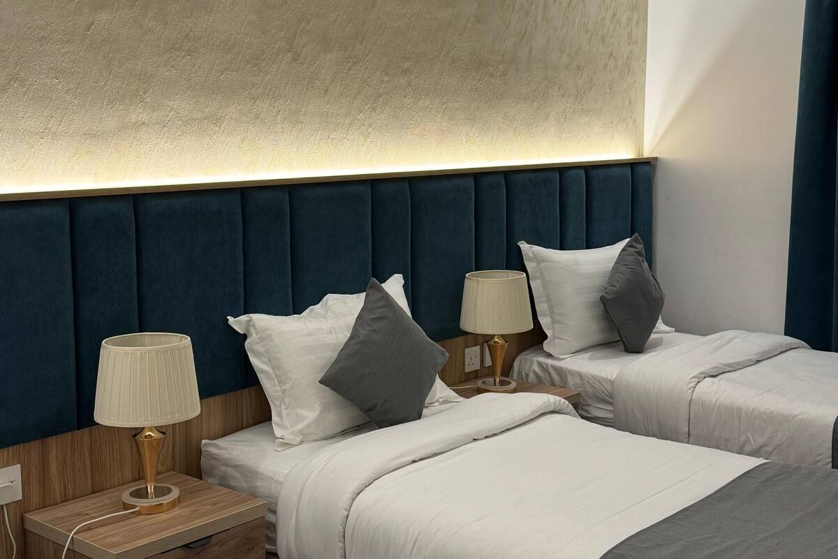 A hotel room with two beds, a wooden nightstand with a lamp, and a textured wall.