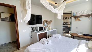 A hotel room with a large bed, a flat-screen TV, a vanity with a mirror, and a small seating area.