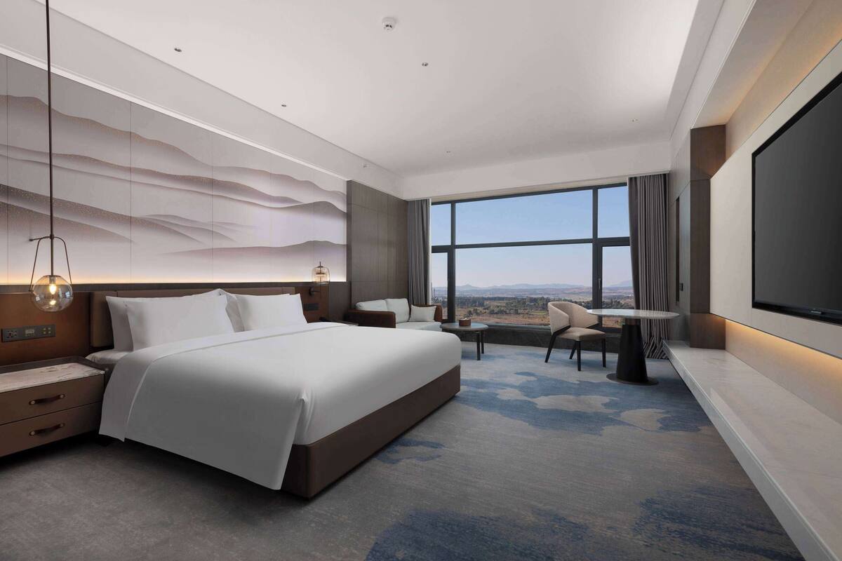 A modern hotel room with a large bed, a desk, and a TV.