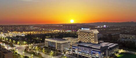 A cityscape at sunset with modern buildings, a prominent hotel, and well-lit streets.