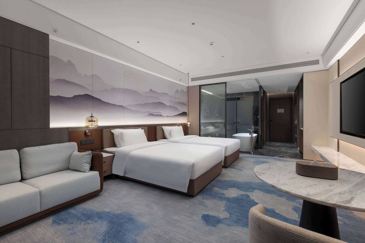A modern hotel room with a large bed, a sofa, a desk, and a TV.