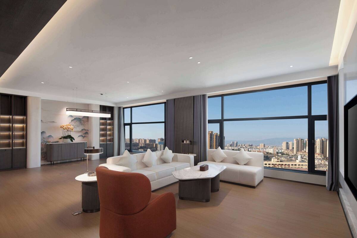 A spacious living room with a modern sofa set, a coffee table, and a view of the city through large windows.