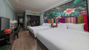 Una habitación de hotel con dos camas, televisor, escritorio y un colorido mural floral en la pared.