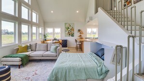 A spacious living area with a large window, a sofa, a dining area, and a staircase. - Kalispell Mountain Getaway w/ Hot Tub & Fire Pit! (Kalispell)