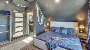 A bedroom with a sloped ceiling, a bed with blue bedding, a bedside table with a lamp, and a wardrobe with a mirror. - Kalispell Mountain Getaway w/ Hot Tub & Fire Pit! (Kalispell)