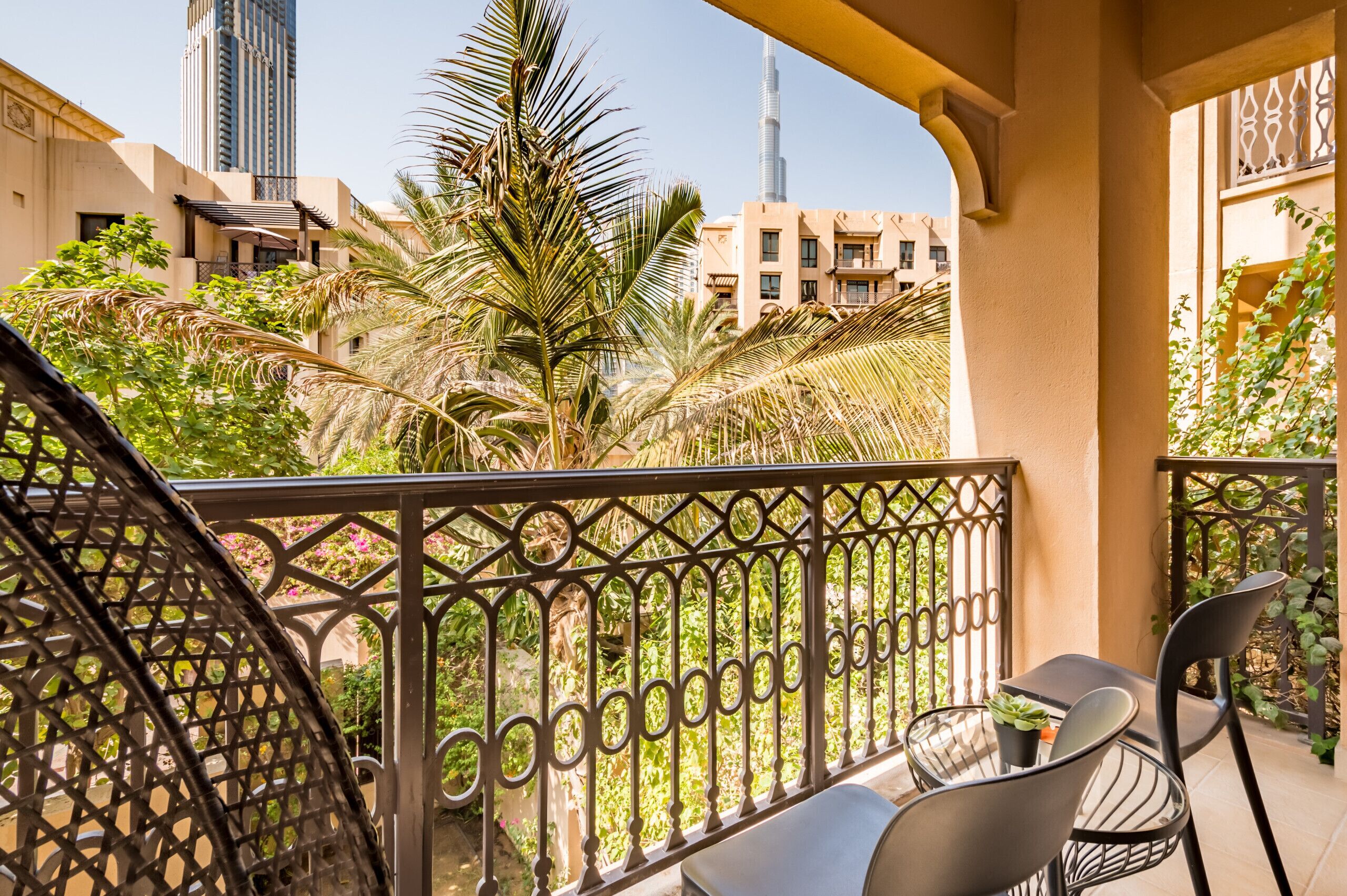A balcony with a wrought iron railing, a table with two chairs, and a potted plant.