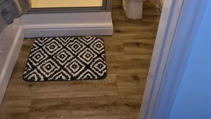 A bathroom with a glass shower enclosure, a toilet, and a patterned rug on the floor. - The Eagle and child  (Preston)