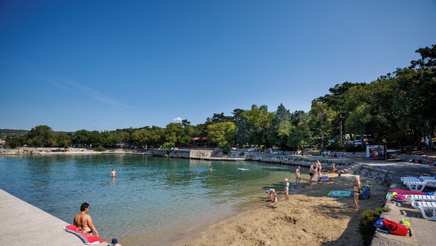 A beach with clear water, people swimming and sunbathing, and beach chairs and umbrellas. - Holiday Homes Oštro (Kraljevica)