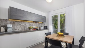 A modern kitchen with white cabinets, a wooden dining table, and black chairs. - Holiday Homes Oštro (Kraljevica)
