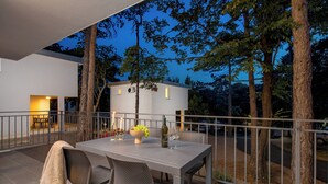 An outdoor dining area with a table and chairs, surrounded by a railing, overlooking a modern house and trees. - Holiday Homes Oštro (Kraljevica)