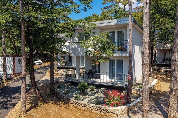 Un bâtiment à deux étages doté de balcons, entouré d’arbres et bordé d’un chemin en pierre.