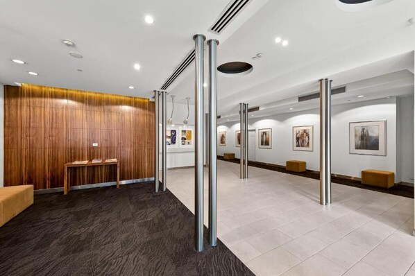 A modern lobby with a reception desk, wooden panel wall, and artwork on the walls. - Readyset Apartments at The Summit (Southbank)
