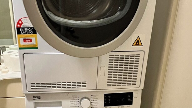 A front-loading washing machine with a front-loading dryer stacked on top. - Readyset Apartments at The Summit (Southbank)