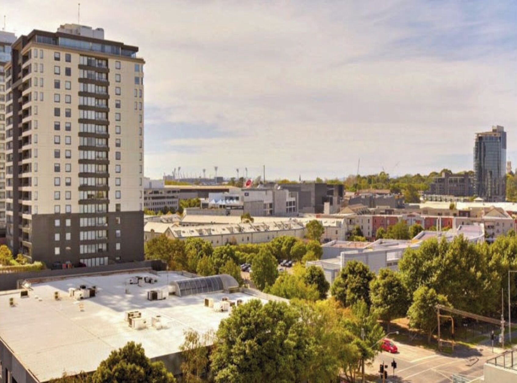 A multi-story building with a flat roof, surrounded by trees and other buildings.