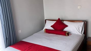 Una cama individual con estructura de madera, ropa de cama blanca y una almohada roja decorativa.