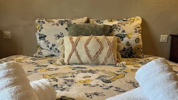 A bed with floral bedding, two pillows, and two rolled towels.