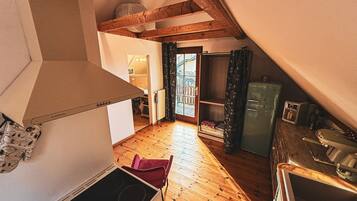 A compact kitchen with wooden flooring, a stove, and a refrigerator.