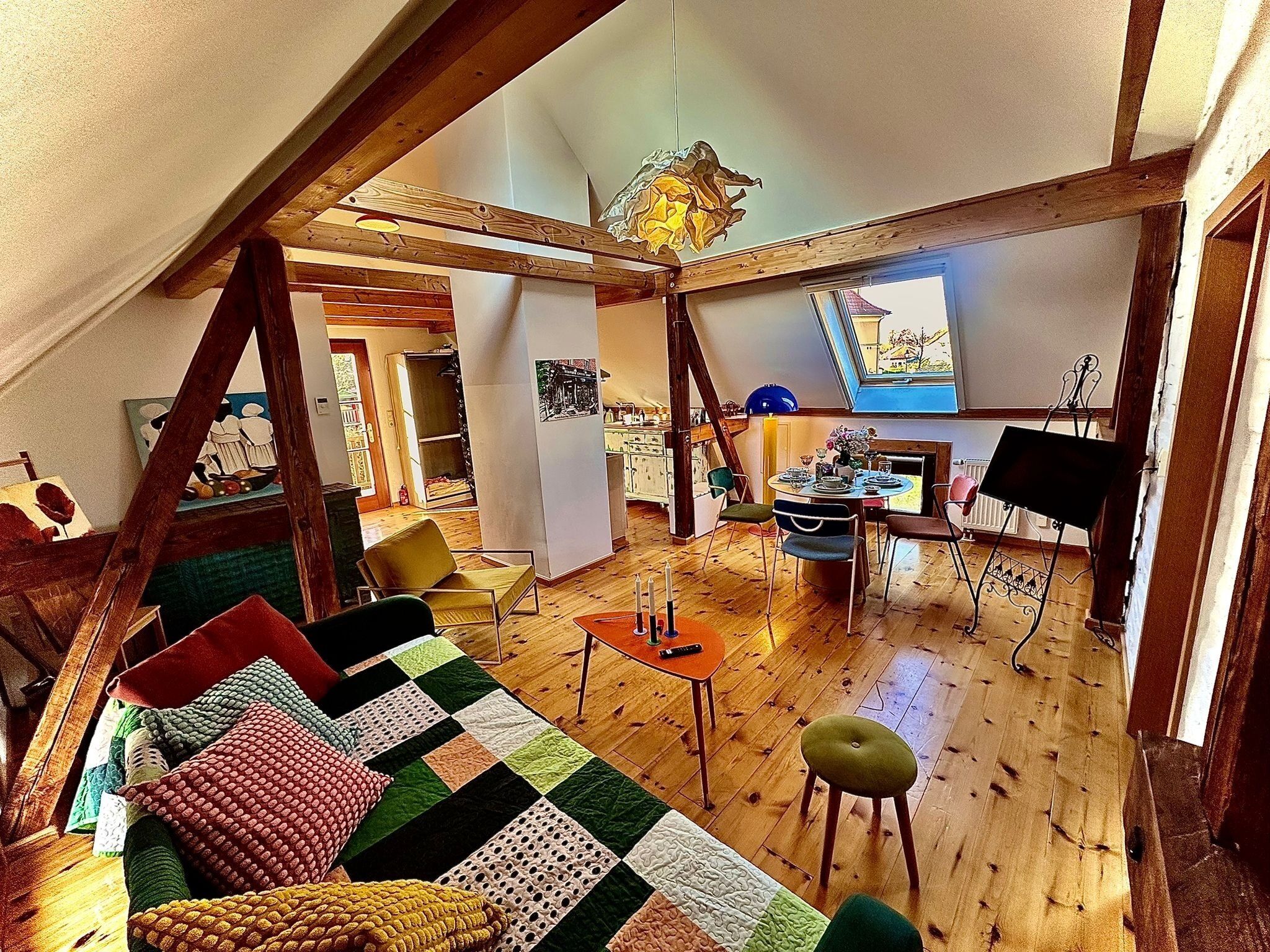Ein gemütliches Loftzimmer mit Holzboden, einem farbenfrohen gesteppten Sofa, einem Esstisch mit Stühlen und einem Klavier.