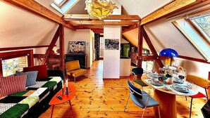 A cozy attic room with wooden beams, a dining table with chairs, a sofa, and a fireplace.