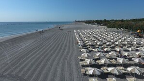 A beach with rows of umbrellas and sun loungers, a sandy shore, and a clear blue sky.