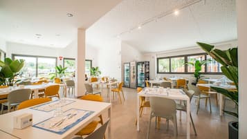 Un vaste espace dédié à la salle à manger, avec des tables et des chaises, de grandes fenêtres et des plantes en pot.