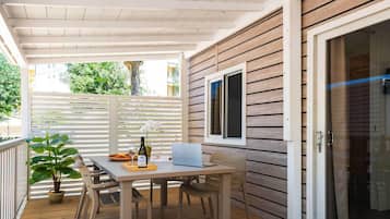 Une terrasse couverte avec une table en bois, des chaises, un ordinateur portable et une plante en pot.