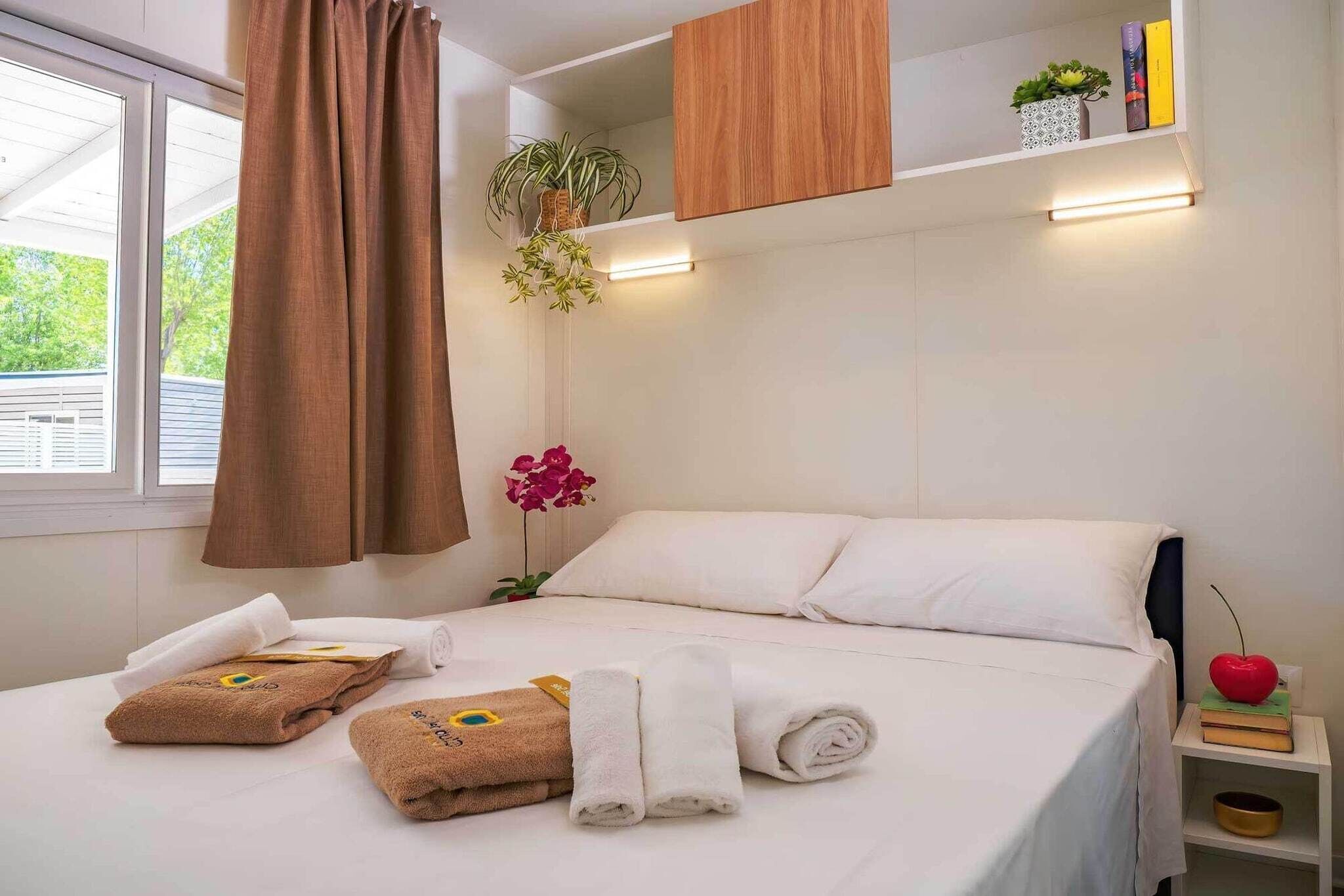 Une chambre d’hôtel avec un lit, des serviettes, une table de chevet, une plante et une fenêtre avec des rideaux.