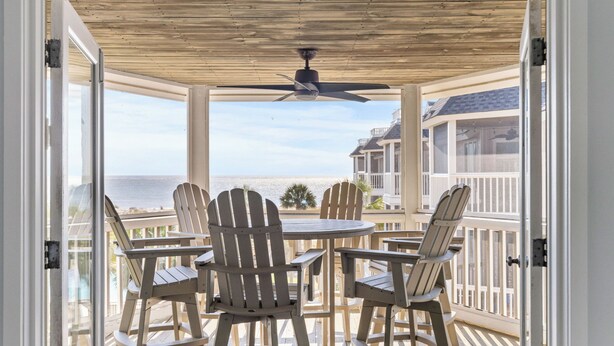 A covered outdoor seating area with Adirondack chairs and a table, overlooking a beach and ocean.