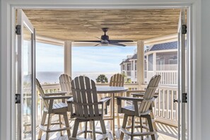 Un espacio de estar al aire libre cubierto con sillas Adirondack y una mesa, con vista a una playa y al océano.