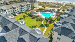 A resort with a large swimming pool surrounded by a well-maintained lawn, a beach view, and multiple buildings with balconies.