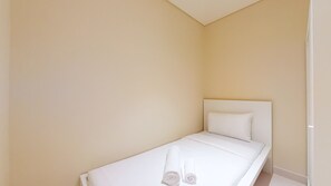 A small, single-bed room with a white headboard and a neatly made bed.